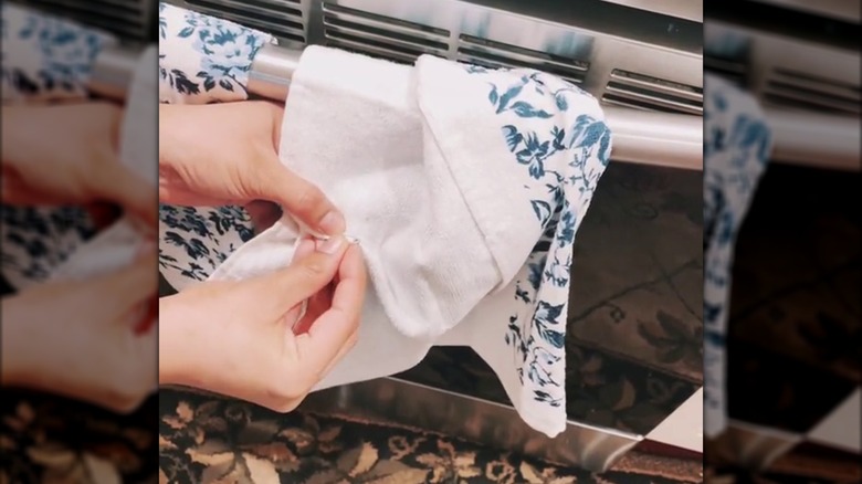 A person using a safety pin to secure a blue and white towel to a handle