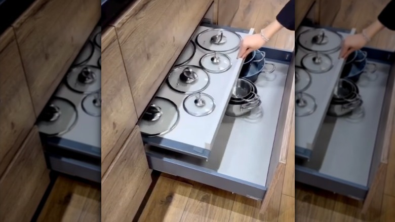 A person pulls a shallow pot lid drawer out over the top of a pot and pan drawer.