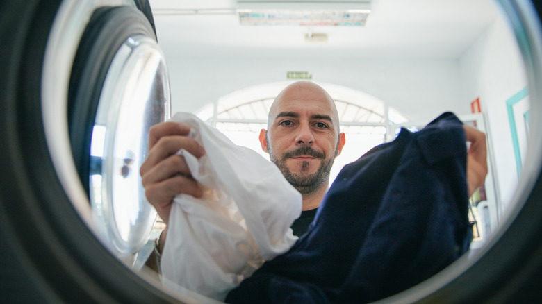 Man loading his bed sheets into the washing machine.