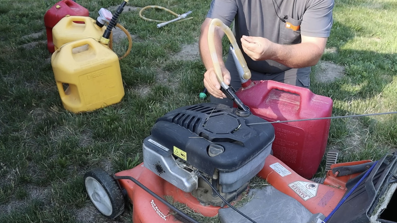 Man uses handheld stick pump to fill up lawn mower.