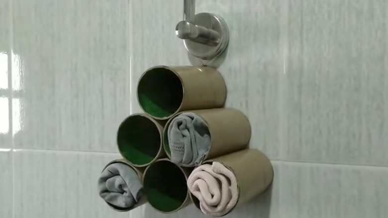 A DIY rag organizer made from toilet paper tubes hangs on a tiled wall.