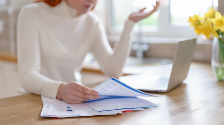 Woman tries to organize the pile of messy paperwork on her kitchen counter.