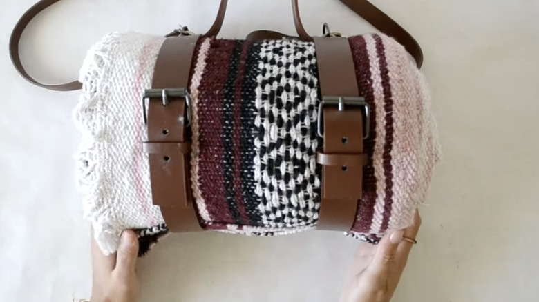 A throw blanket rolled up and wrapped in leather straps ready to hang in a closet.