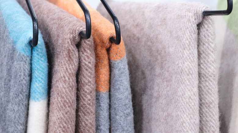 Several colorful blankets on clothes hangers in a row.