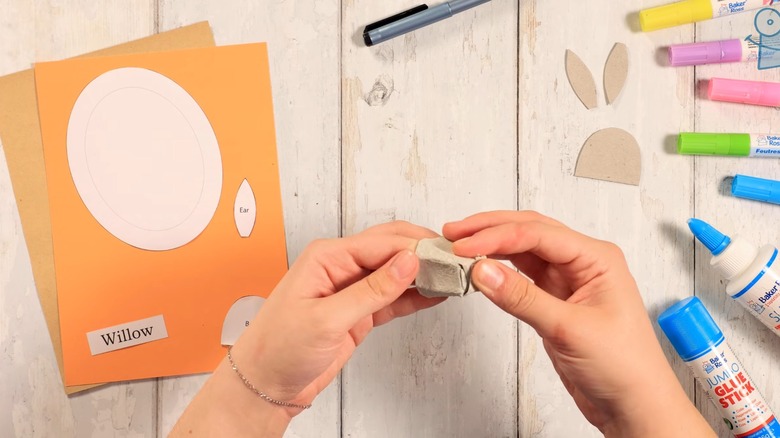 Hands folding a cut cone from an egg carton into a rabbit's snout