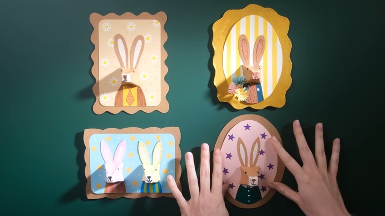 Hands hanging decorated bunny portraits on a green wall
