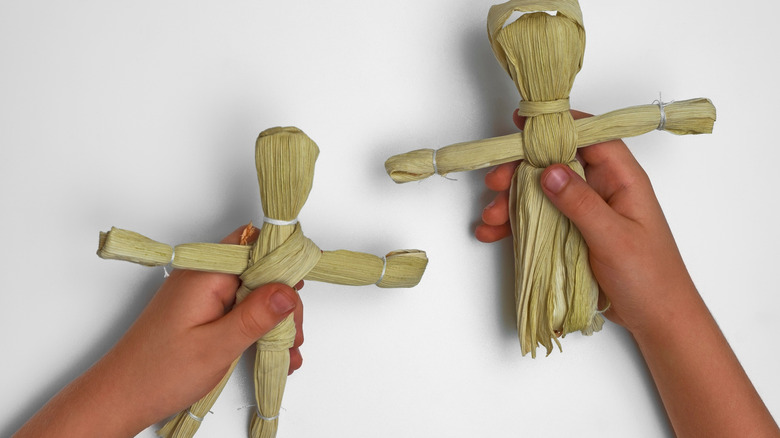 Close up of child holding two corn husk dolls