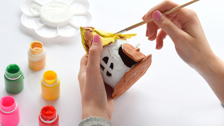 A person's hands up close as they paint a homemade fairy house.