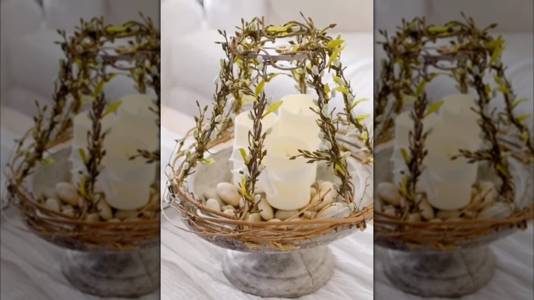 A bell-shaped lampshade frame wrapped with faux greenery and put on tabletop bird bath.