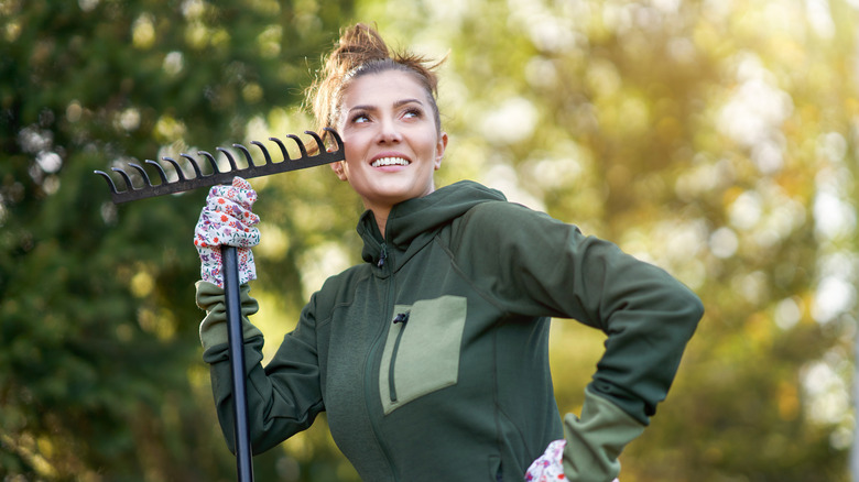 A woman stands holding a rake, looking away with an idea in her head