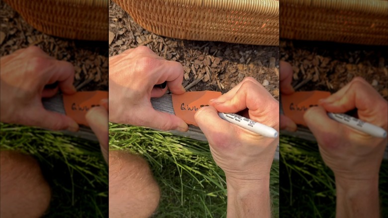 Hands writing on clay pot shard on edge of raised wooden garden bed