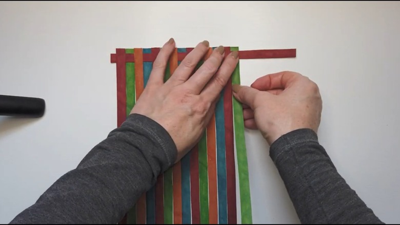 Demonstrator hand-weaving cardboard strips into a placemat design