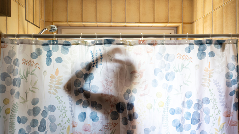Silhouette of a person behind white shower curtain with a botanical pattern