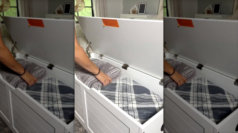 Woman placing folded blankets into a storage trunk.