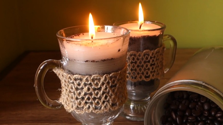 Lit candles in glass coffee mugs on a wood surface