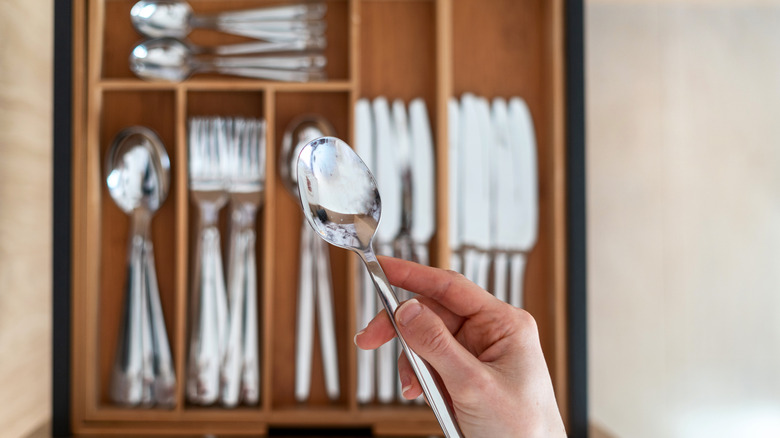 A person holding a spoon above a bamboo silverware organizer