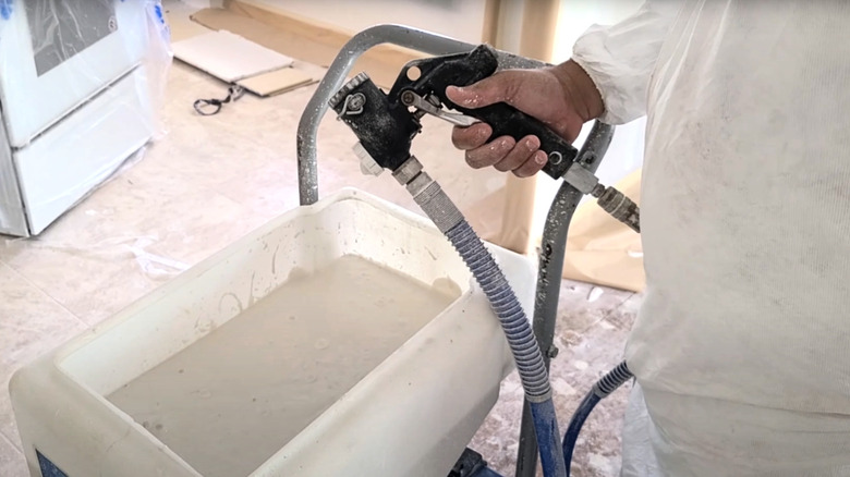 Man holding texture sprayer system in covered indoor room