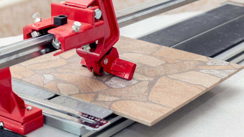 Red tile cutter slicing through masonry style porcelain tile