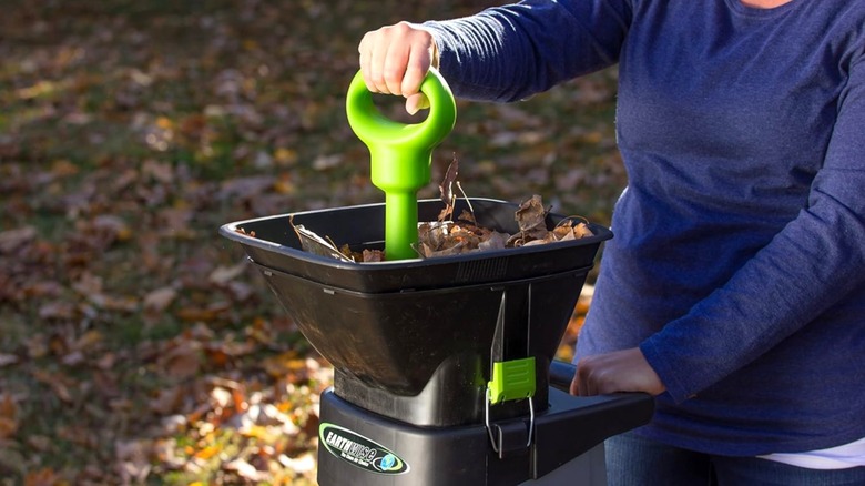 Woman operating wood chipper with green handle in yard with fallen leaves