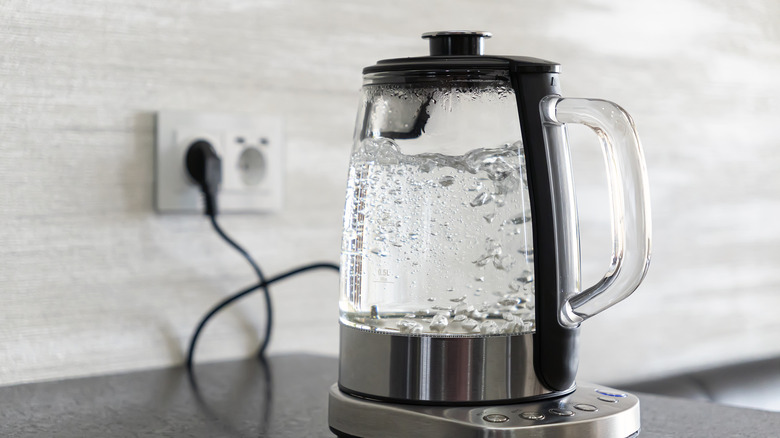 Electric glass teakettle with water boiling inside.