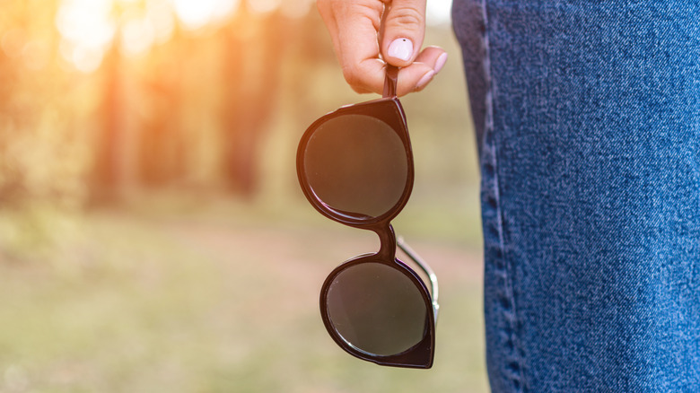 Person holding a pair of black sunglasses next to leg