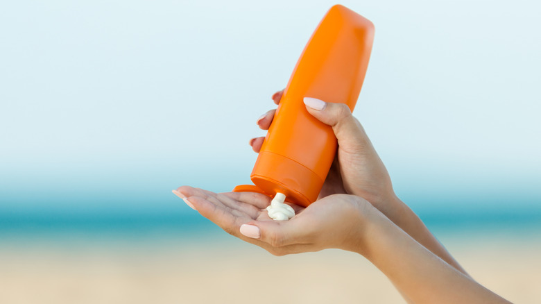 Hands dispensing an orange bottle of sunscreen