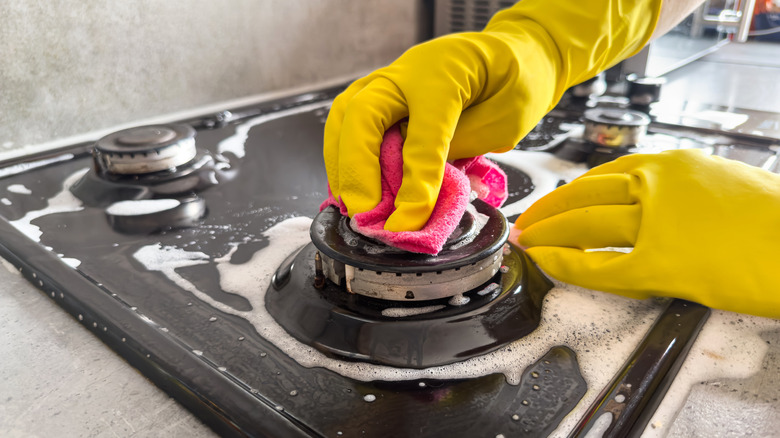 Close up of person wearing gloves cleaning a gas stovetop burner