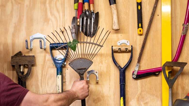 person reaching for tools on garage wall