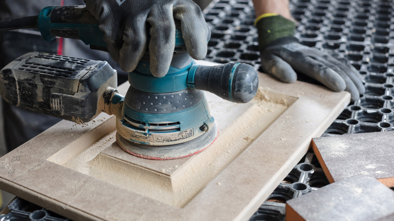 A carpenter sands wooden furniture facades with a sanding machine at a furniture production factory