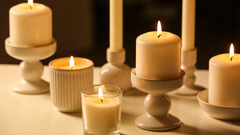 Several lit white pillar and jar candles are arranged on a table.