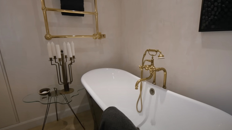 Stylish bathtub with vintage gold fixtures, antique candelabra, and gold towel rack