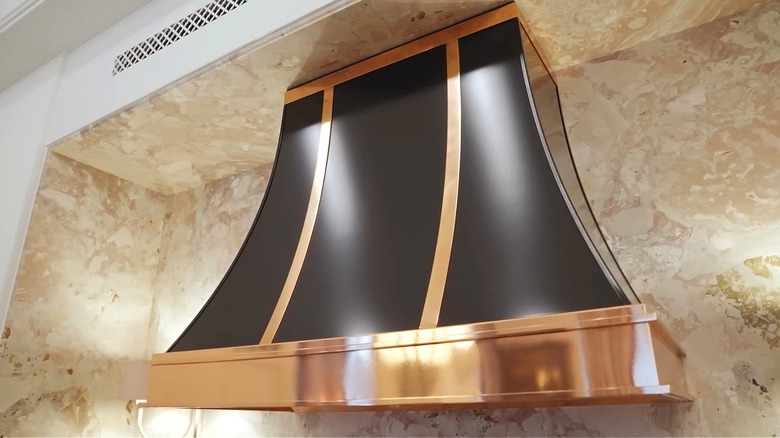 A black and copper hood attached to a beige marble wall.