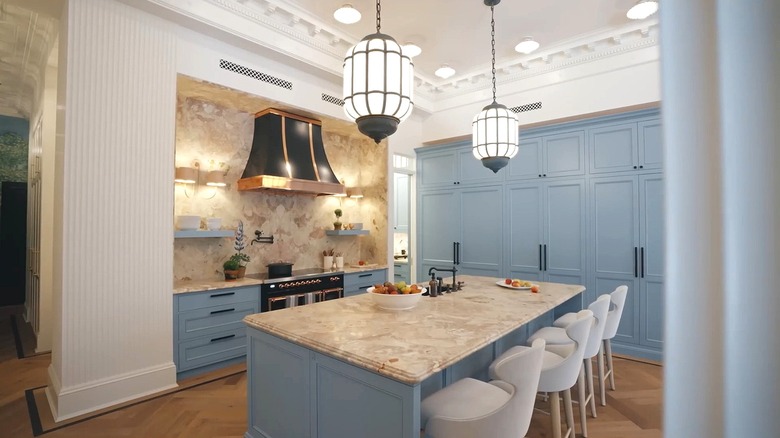 Kitchen with baby blue cabinets, and beige countertops and backsplash. White chairs and black and white ceiling lamps.