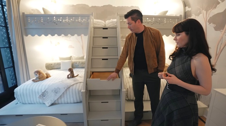 Man and woman stand in a children's room. Man opens drawer in one of the steps of the bunkbed.