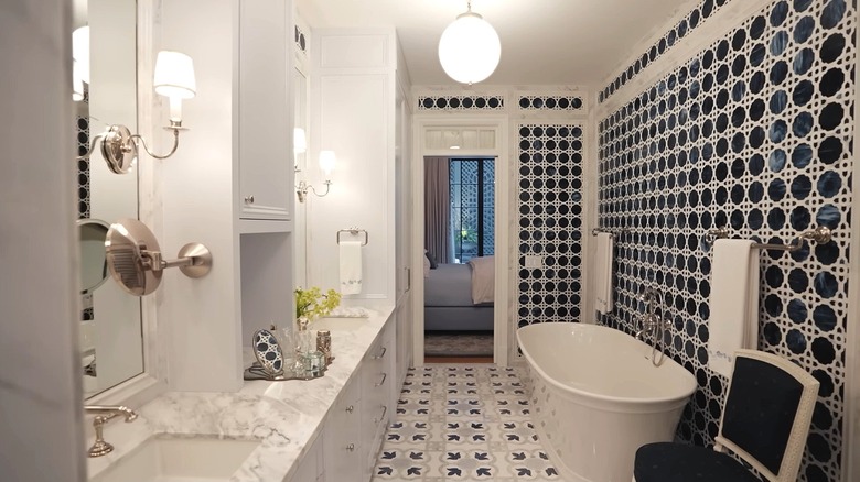 Bathroom with glass wall tiles, mosaic floors, marble countertop and a white freestanding bathtub.