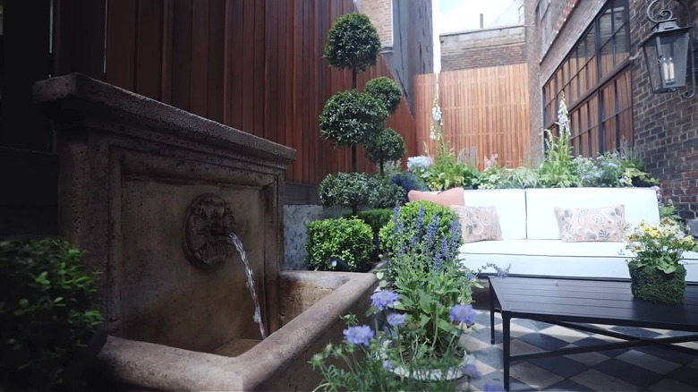 A terrace with checkerboard stone floor, a white sofa, and a stone fountain.