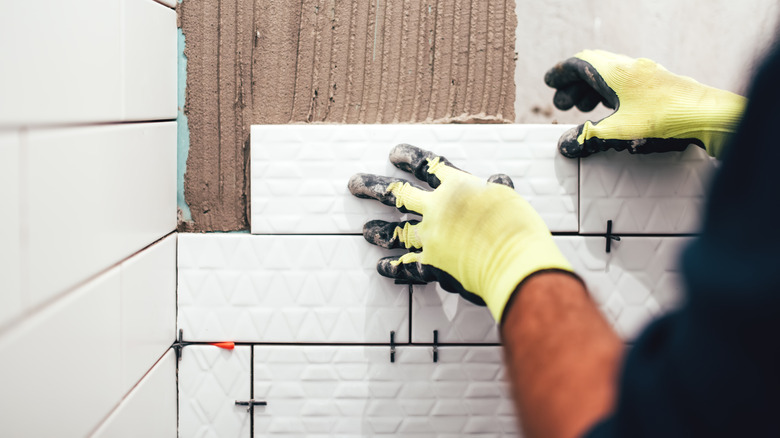 person installing white subway tiles