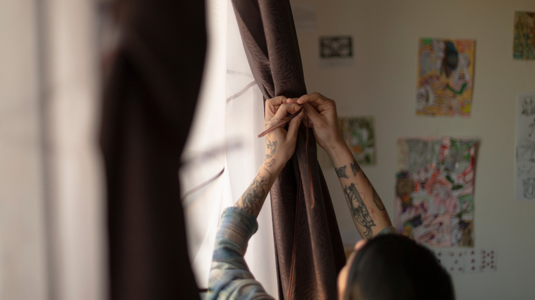 A person adjusts a tie on a brown curtain