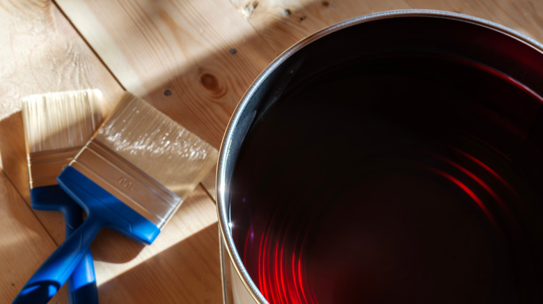 Two paint brushes are sitting next to a dark wood varnish