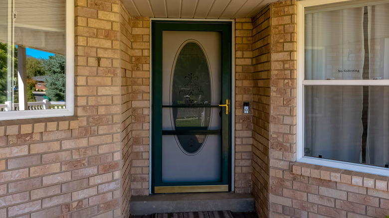 A black screen door on a light brick house