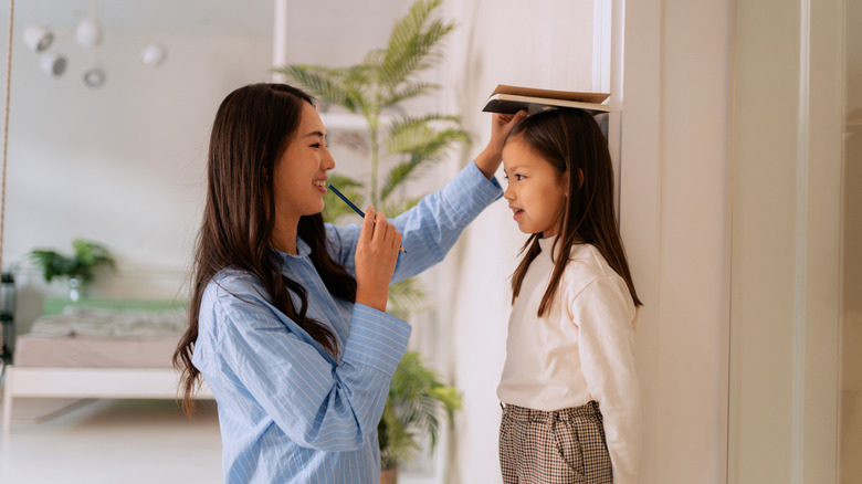 Mother measures daughter's height on door frame