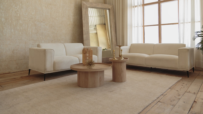 Living room with damaged floor decorated with beige couches, rug, and mirror