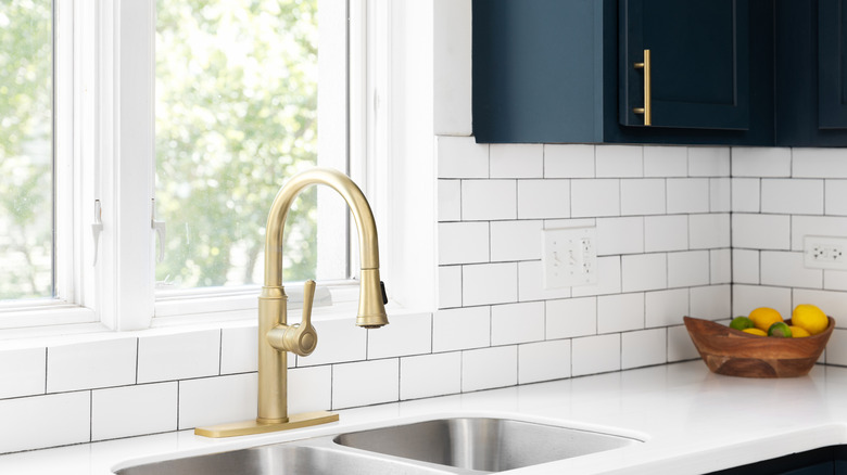 A brass kitchen sink surrounded by white subway tile on the backsplash