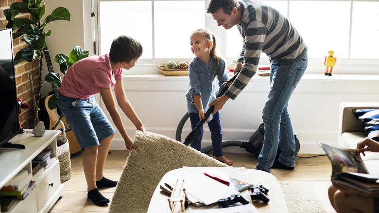 Children helping their father vacuum a rug