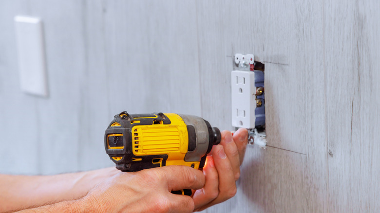 A wall outlet with surge protection is being installed by a maintenance man with an electric drill