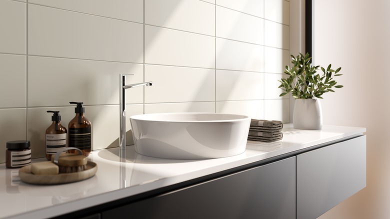 View of bathroom with white tile backsplash, white countertop, and black cabinets.