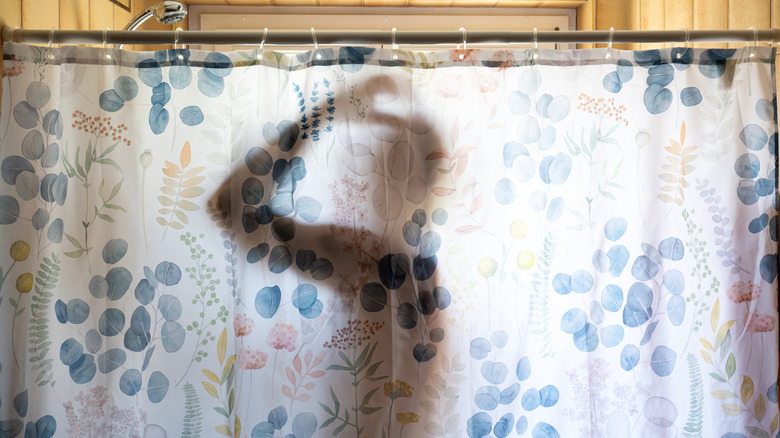 The silhouette of a person in the shower behind a floral shower curtain