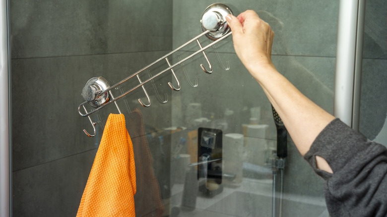 Woman removing towel rack with hook from shower door.