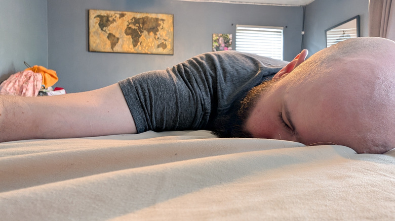 Bald man laying face down on comfortable mattress with cream-colored sheets