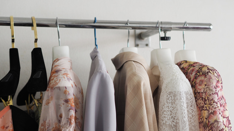 Various pieces of clothing hang on metal hangers in a closet.